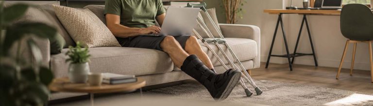 Mann mit verletztem Bein arbeitet zu Hause am Laptop
